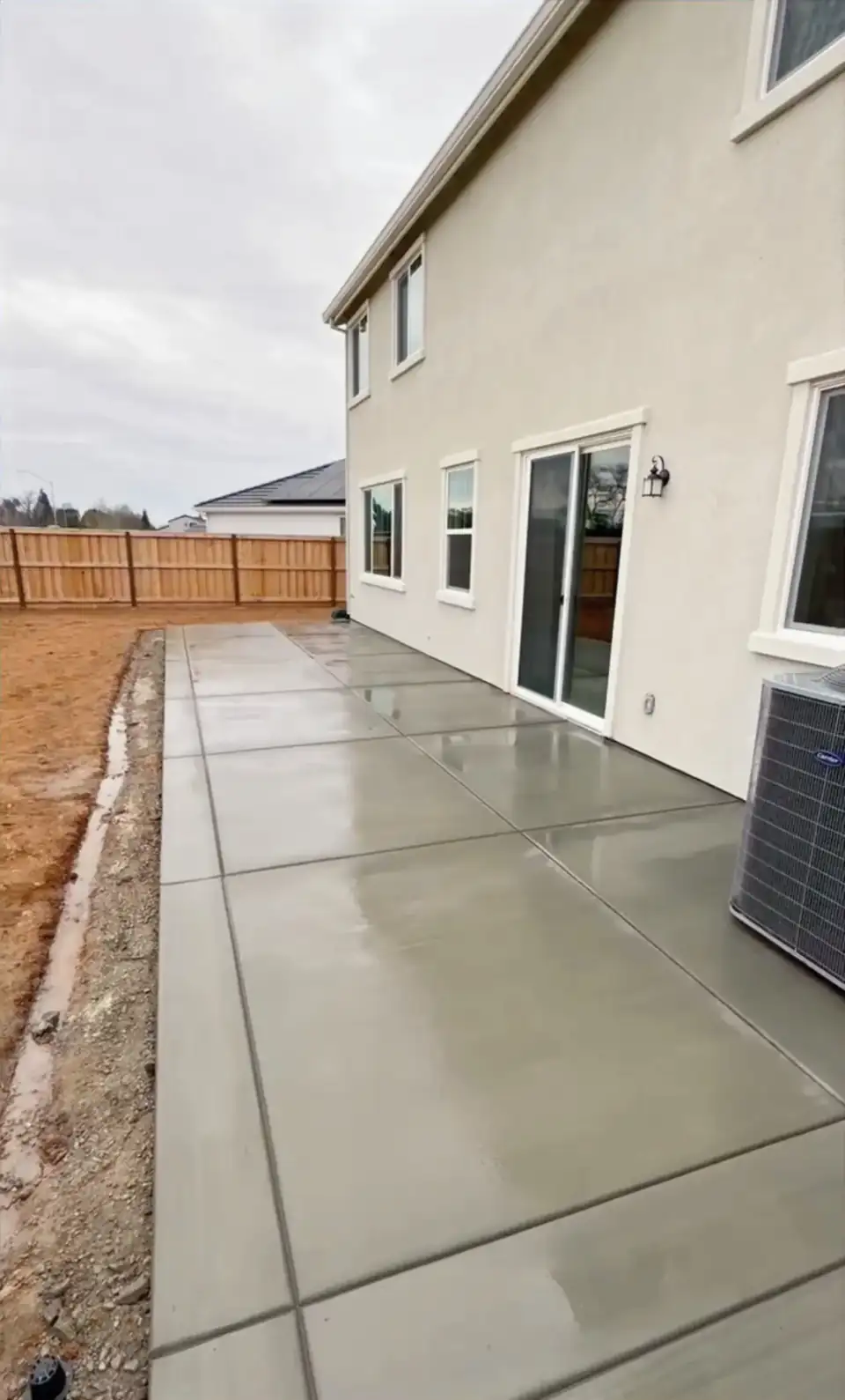 Finished concrete path running between a two-story home and a wood fence